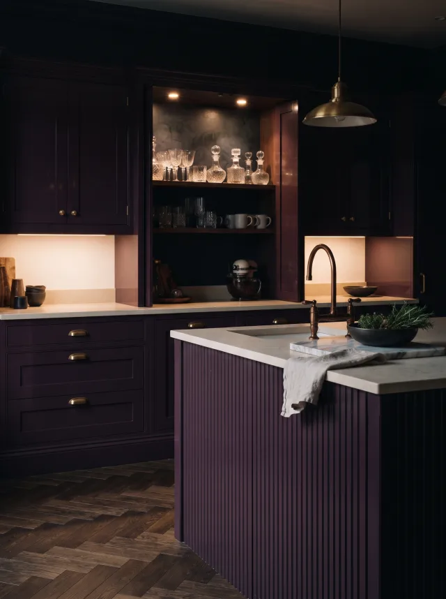 Deep aubergine kitchen with glossy plum cabinets, a fluted island, antique gold handles and limestone tops