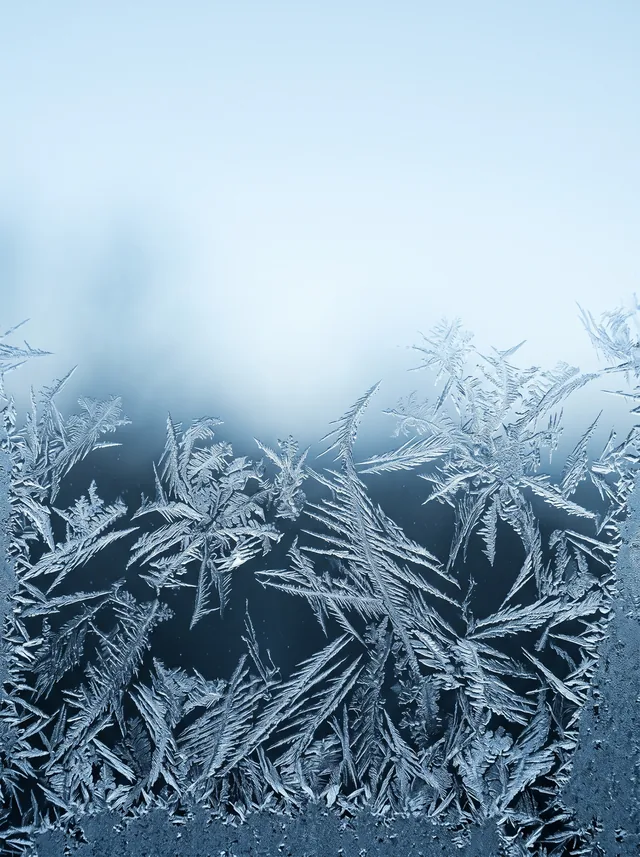 Frost crystals on dark glass backlit by cold blue dawn light in ice white and glacier blue