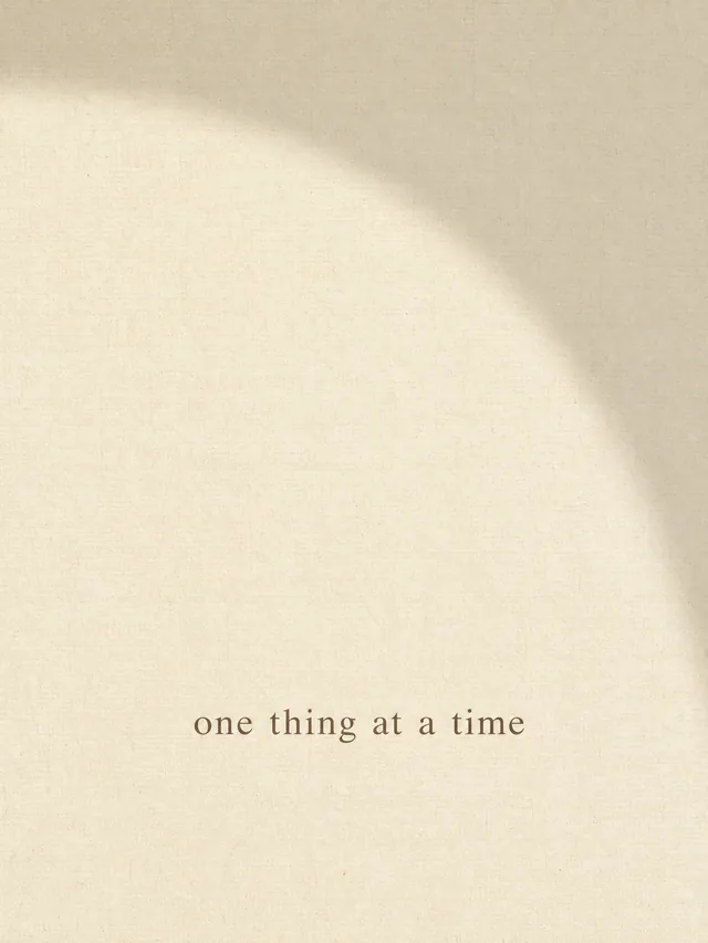Minimalist cream phone wallpaper with a linen texture and the phrase one thing at a time in a sepia serif